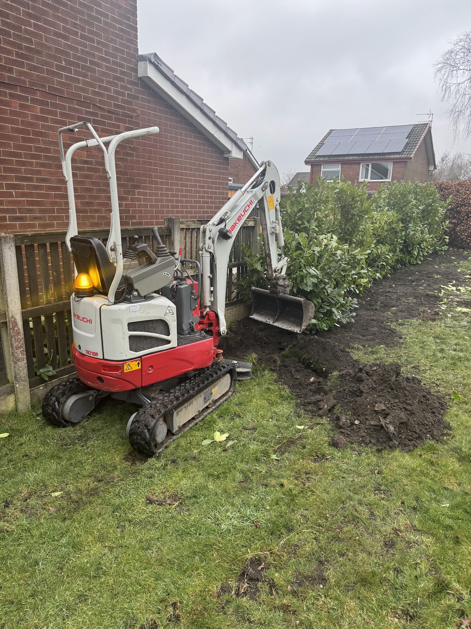 Mini digger clearing ground beside a house during a garden and tree clearance job
